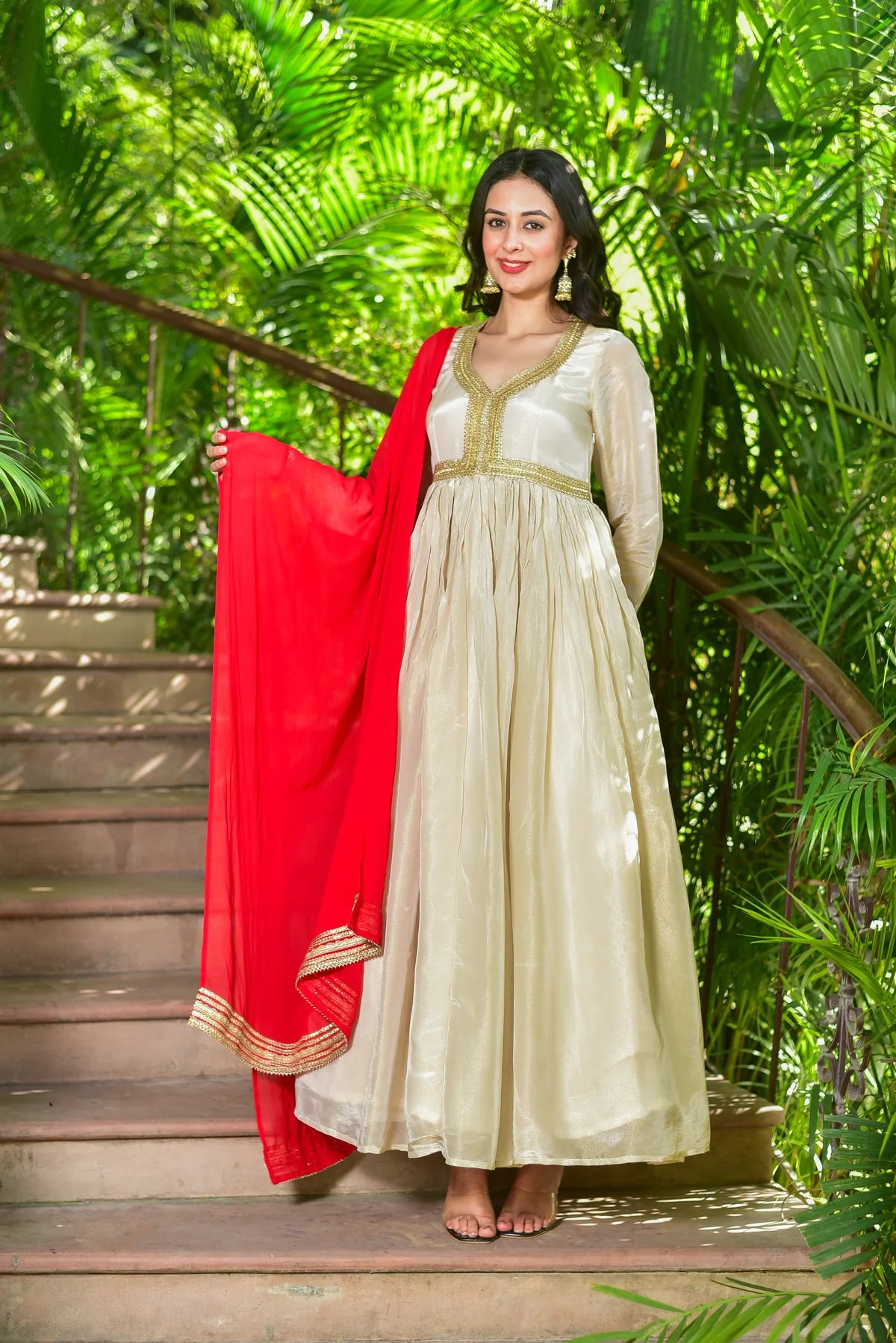 Experience regal elegance with The Shahi Silk Anarkali Set – a luxurious 2-piece ensemble that embodies timeless grace and festive grandeur. This stunning set features a flowing anarkali dress in rich cream zari silk with exquisite gold lace detailing, paired with a vibrant red chiffon dupatta for a truly majestic look.