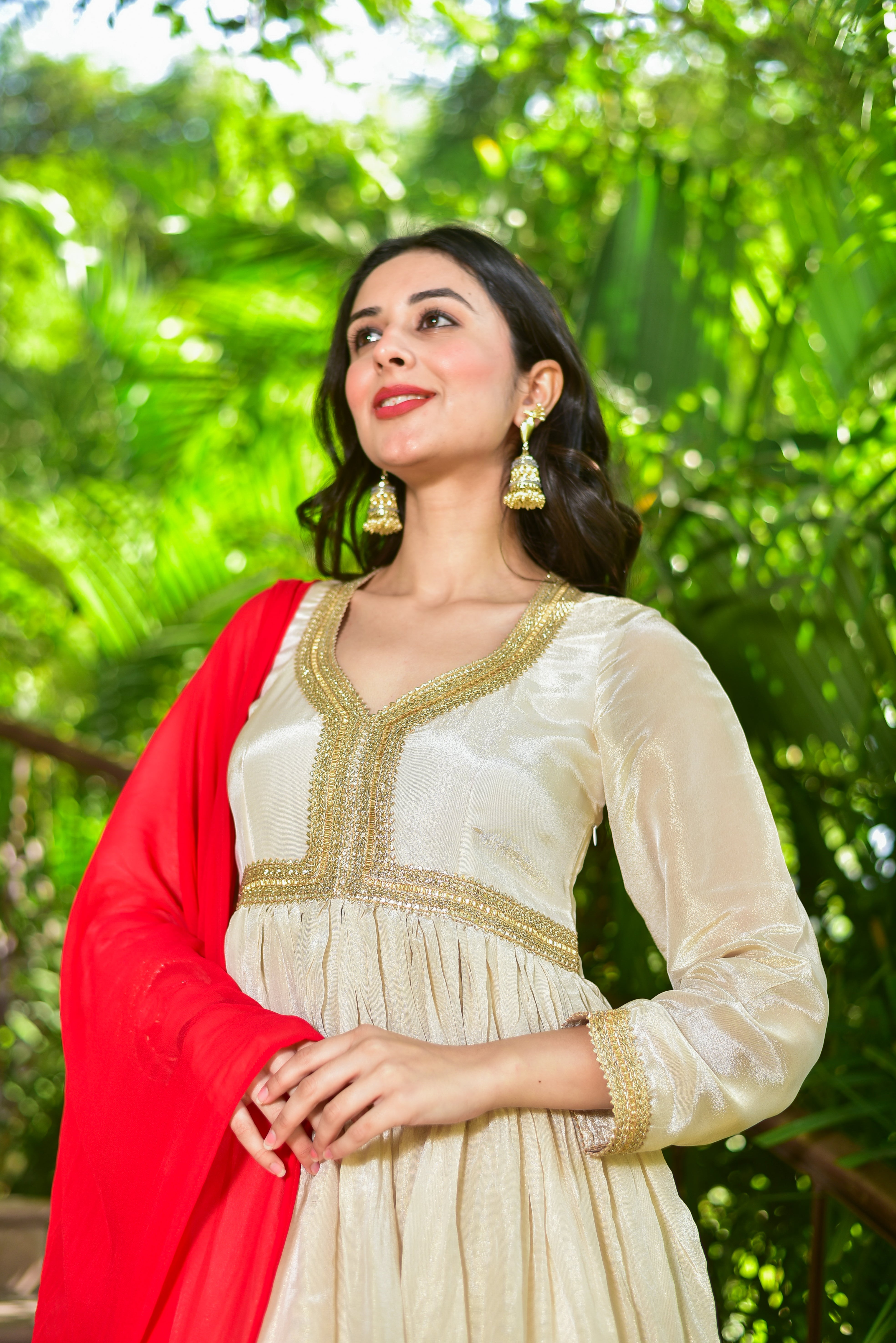 Woman in a traditional outfit with a red shawl against a green leafy background